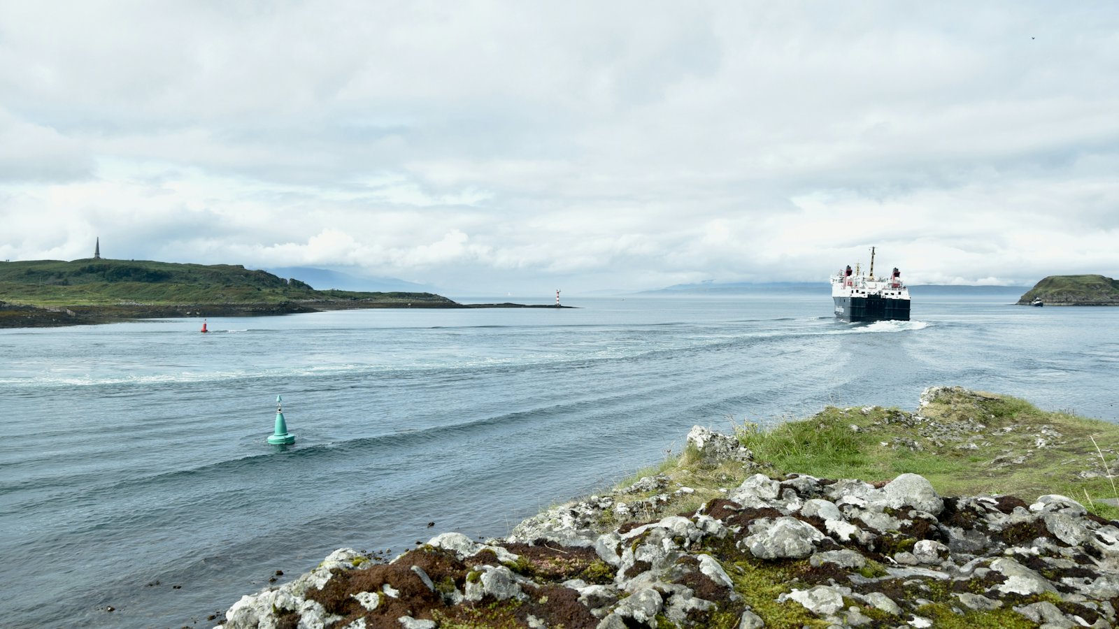 A car ferry crossing open water with hills behind
