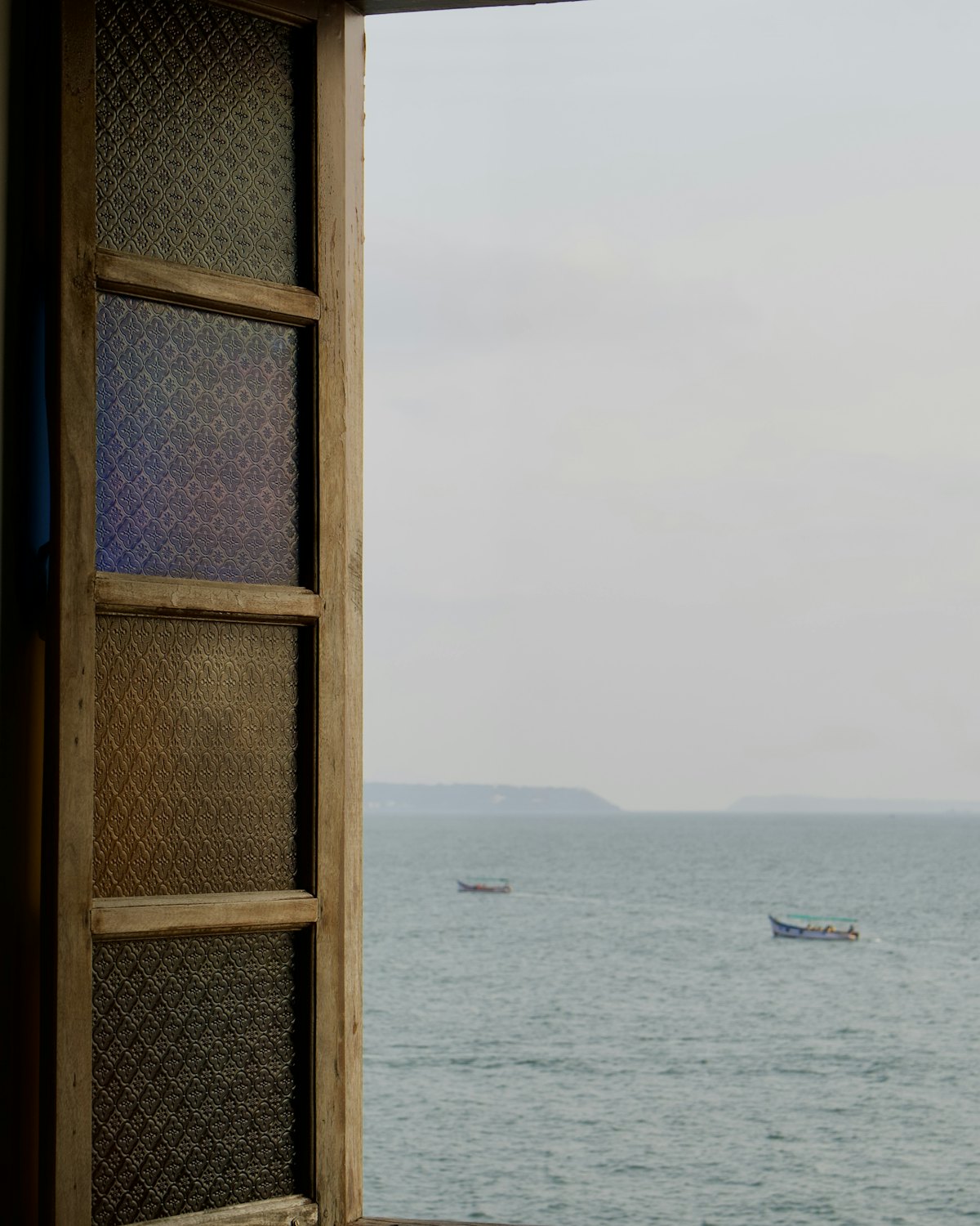 Sea and small boats seen through an open window with old glazed shutters